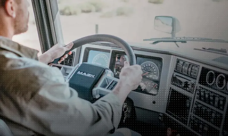 Conductor al volante de un camión de carga pesada con vista del tablero digital y controles Mack.