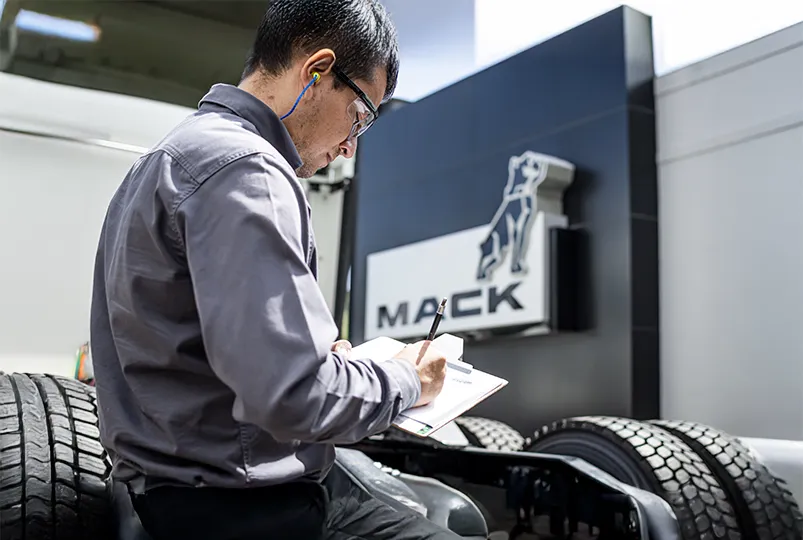Inspector técnico llenando una lista de verificación de mantenimiento junto a un camión Mack.