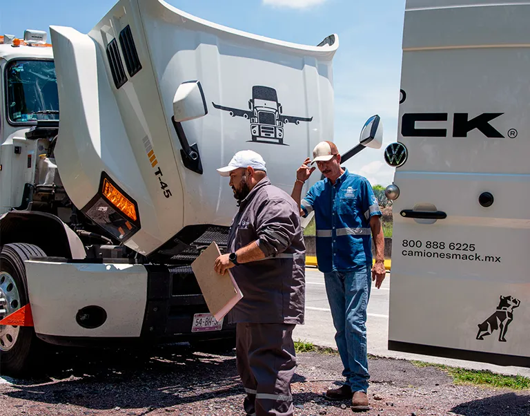 Técnico de servicio especializado revisando un camión Mack con el cofre abierto en carretera.