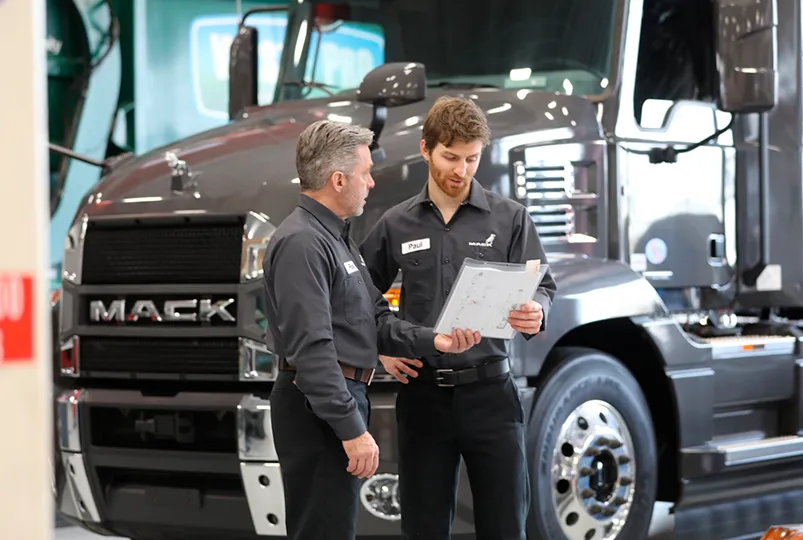 Asesores de servicio tecnico revisando un diagrama de diagnostico frente a un camion de carga pesada.