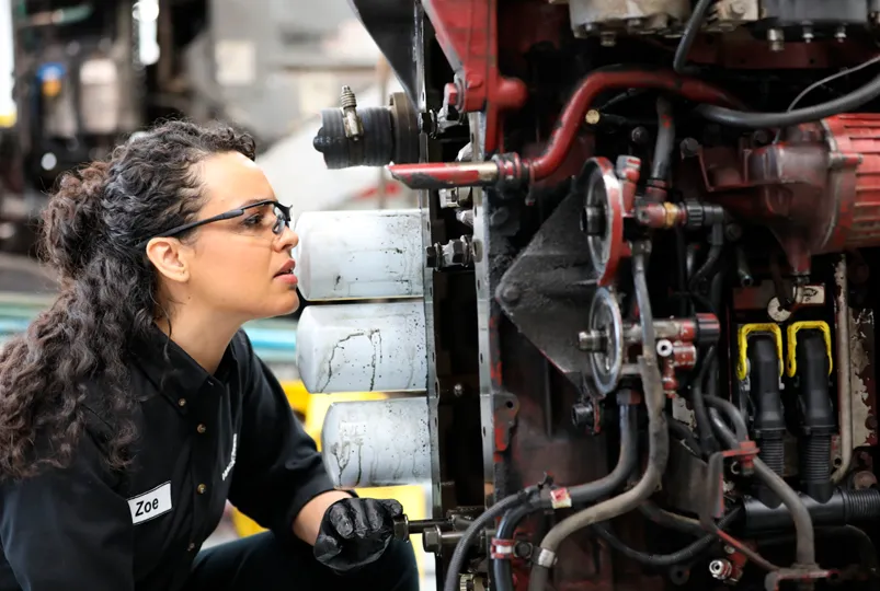 Tecnica automotriz especializada inspeccionando filtros de aceite y componentes en un motor diesel pesado.